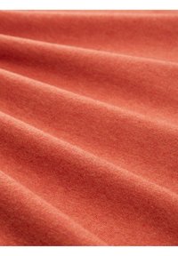 Tissu de couleur rouille avec une surface douce et texturée, présentant de subtils ondulations et plis. Le matériau semble chaud et confortable.