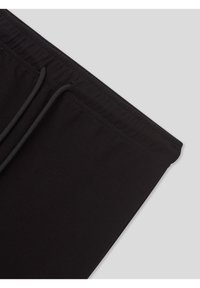 Pantaloni della tuta neri con vita a coulisse e texture liscia. Angoli inferiori arrotondati e dettagli di cuciture semplici.