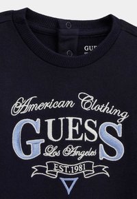 Marineblauer Sweatshirt mit geripptem Rundhalsausschnitt, bestickt mit weißem und hellblauem Text: "American Clothing GUESS Los Angeles EST.1981."