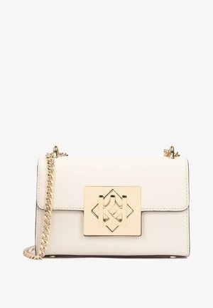 Crop top blanc à pois avec une épaule et un détail floral, associé à un pantalon noir taille haute et des sandales à talons blocs dorés.