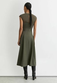 Rohelist oliivivärvi kleit koos kapuutsvarrukatega, liibuv vöökoht, lõhenev seelik ja seljal võtmeauguga avaus. Kaasas põlveni ulatuvad mustad saapad.