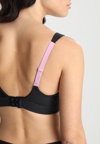 Svart BH med justerbare rosa stropper og krok lås, med en glatt tekstur og små utskjæringer på båndet.