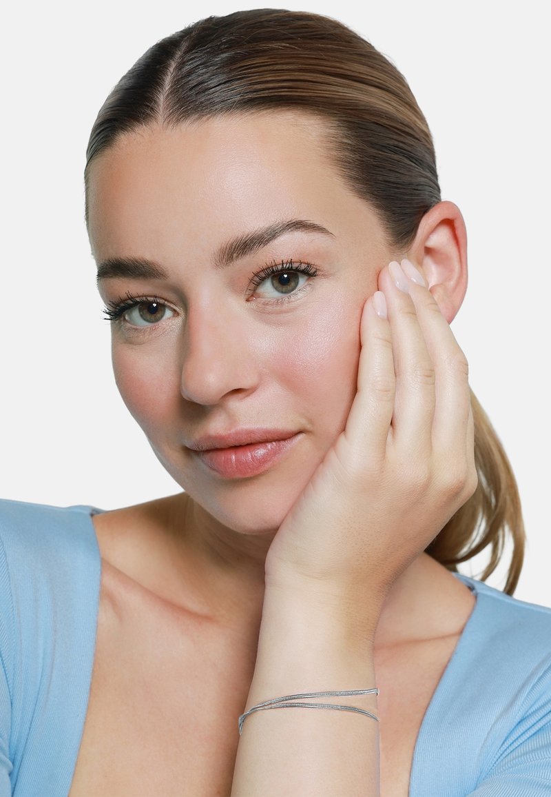 Modella con pelle chiara e capelli castani, che indossa un top blu. Mostra un bracciale d'argento, con un design liscio ed elegante, su uno sfondo bianco.