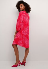 Röd klänning med paisley-mönster i medellängd, puffärmar och löst snitt. Kombinerad med rosa högklackade slingback-skor.