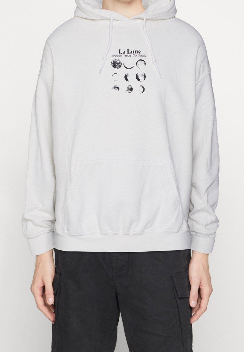 Ljusgrå hoodie med en frontficka. Har en svart grafisk tryck av månens faser och texten: "La Lune, En guide genom vår galax."