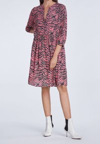 Robe rayée zèbre rose et noire avec des manches trois-quarts, un col en V et une taille élastique. Portée avec des bottines blanches.