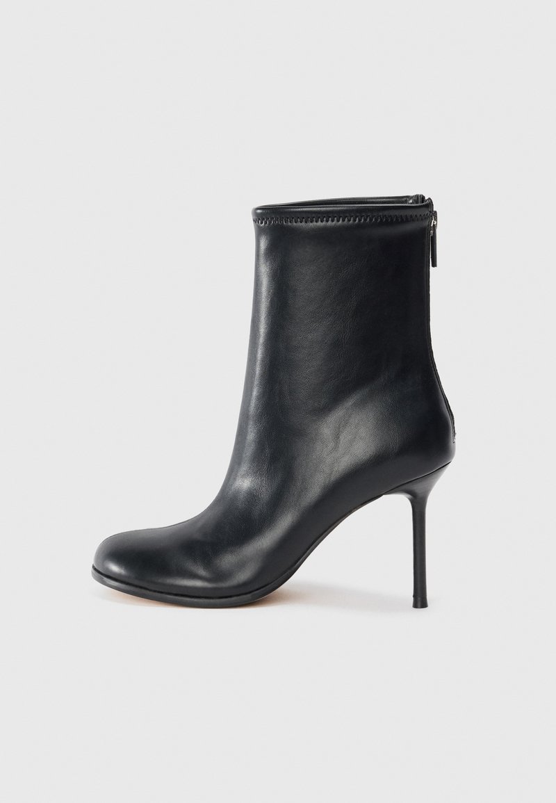 Černá kožená kotníková bota s špičatou špičkou, štíhlým vysokým stiletto podpatkem a zipem na zadní straně.