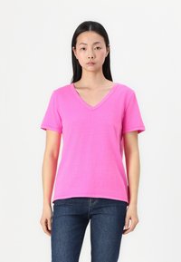 Tricou roz cu mânecă scurtă și guler în V. Fabricat dintr-un material moale, având o croială lejeră și detalii de coasere minime.