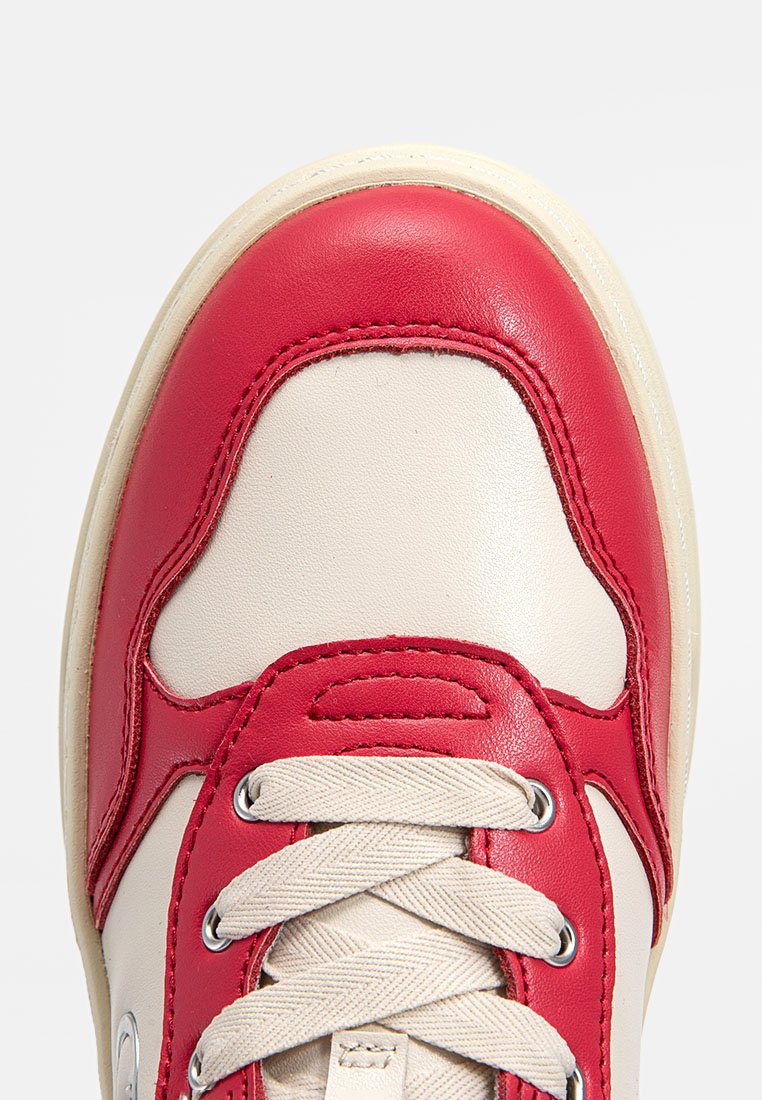 Zapatilla de cuero crema con acentos rojos, puntera redondeada y parte superior texturizada. Presenta cordones beige y ojales plateados. Superficie suave, diseño casual.