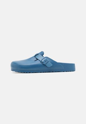 Zuecos de goma azules con punta redondeada, correa ajustable y suela texturizada. Acabado liso sin patrones ni acentos visibles.