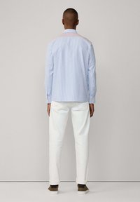 Camicia a righe blu chiaro con maniche lunghe e colletto con bottoni, abbinata a pantaloni bianchi, indossata da una persona vista di spalle.