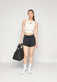 Witte cropped tanktop met zwart logo, zwarte sportshorts, witte sneakers en zwarte sporttas. Eenvoudig ontwerp, gladde textuur.