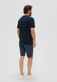 Marineblauwe katoenen T-shirt met korte mouwen, gecombineerd met donker gestreepte shorts en witte sneakers, bekeken van achteren.