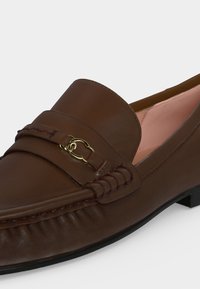 Mocassin en cuir marron avec détail mors en métal doré, coutures cousues et doublure intérieure rose clair.