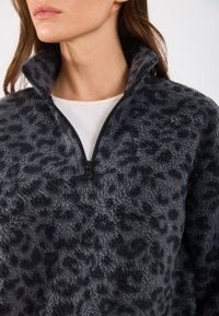 Pulover din fleece de culoare gri închis, cu un model texturat de leopard. Are un guler cu fermoar pe jumătate și o textură moale, pufoasă. Design simplu, versatil.