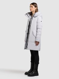 Gaiši pelēka pūka jaka ar augstu apkakli, priekšējām aizdares pogām un sānu kabatām. Valkāta kopā ar melnām legingām un masīvām melnām zābakiem.