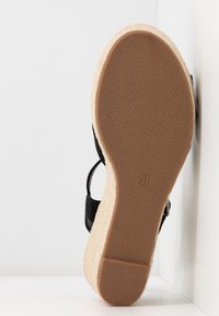 Sandale noire avec une semelle en cuir texturé marron, design d'espadrille en jute surélevé, lanières réglables, indication de taille "37" embossée au fond.