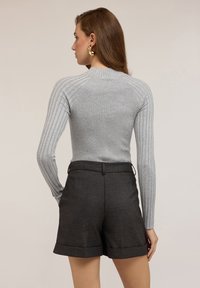 Maglietta grigia a maniche lunghe con design aderente, abbinata a pantaloni corti a quadri scuri, caratterizzati da orli risvoltati e una vita liscia.
