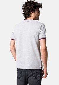 Szara koszulka polo z krótkim rękawem, z żebrowanym kołnierzykiem w czerwone i granatowe akcenty oraz logo z tyłu. Wykonana z miękkiej bawełny.