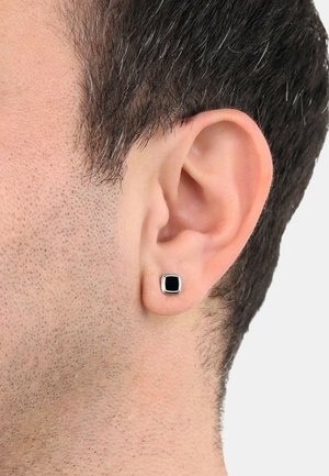 Schwarze quadratische Ohrstecker mit silberfarbigem Rahmen, getragen in einer kurz geschnittenen Frisur, die die glatte Textur gegen die Haut zur Geltung bringt.