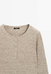 Pull en tricot côtelé beige avec un col rond et cinq boutons recouverts de tissu à l'avant. Texture douce avec un motif chiné subtil.