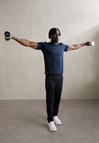 Black athletic pants, navy fitted t-shirt, white sneakers; individual using dumbbell in each hand with arms extended horizontally.