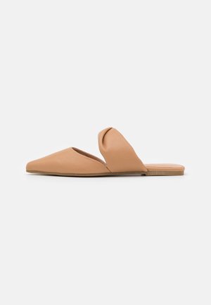 Flad tan slip-on sko med spids tå og en bred, foldet rem over toppen, vist på en ensfarvet hvid baggrund.