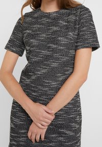 Svartvit texturerad klänning med korta ärmar och rund halsringning, med ett vävt mönster och en figurnära siluett.