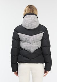 Black puffy jacket with a patterned gray hood and chevron design on the back. Features a lightweight, insulated material and a casual cut.