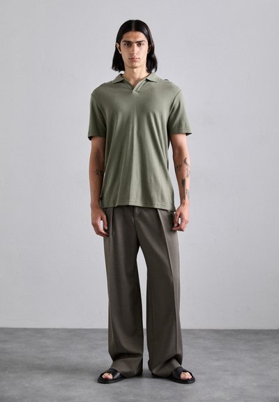 Polo shirt vert olive avec un col, associé à un pantalon noir ample. Porté avec des sandales noires. Texture lisse, design décontracté.
