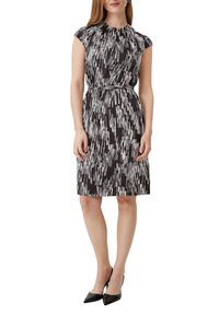 Schwarzes Kleid mit diagonalen weißen Linienmustern, kurzen Kappärmeln, gerafftem Ausschnitt, tailliert und knielang, kombiniert mit schwarzen High Heels.