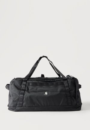 Čierna Carhartt taška typu duffel s dvojitými rukoväťami, predným vreckom na zips a obdĺžnikovým tvarom na jednoduchom bielom pozadí.