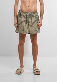 Shorts leggeri con motivo mimetico, dotati di una cintura elastica e di una piccola etichetta con logo di lato. La combinazione di colori presenta tonalità terrose.
