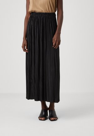 Falda maxi negra plisada con cintura elástica, combinada con zapatos de tacón abiertos negros. Textura suave, diseño de largo completo.