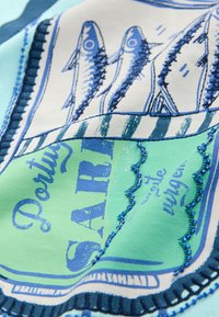 Tkanina o zielonym tle z niebieskimi ilustracjami ryb, ozdobiona niebieskim dekoracyjnym przeszyciem i nadrukowanym tekstem.