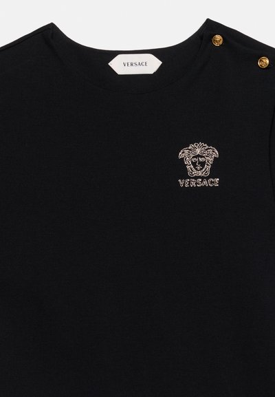 Μαύρο τοπ Versace με στρογγυλή λαιμόκοψη, χρυσλό λογότυπο κεφαλής Μέδουσας και όνομα της μάρκας στο στήθος, καθώς και δύο χρυσά κουμπιά στον ώμο.