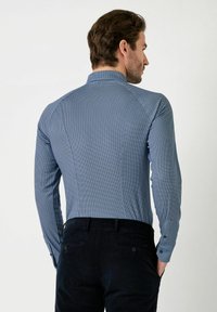 Langarmshirt in klein blauw en wit geometrisch patroon, katoenmix stof, met knoopmanchetten, nauwsluitend ontwerp, gecombineerd met donkere corduroy broek.