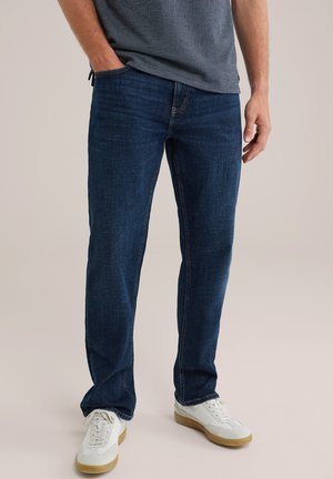 Vaqueros de mezclilla azul con corte recto, con bolsillos frontales y detalles de costura sutiles. Combinados con zapatillas deportivas blancas.