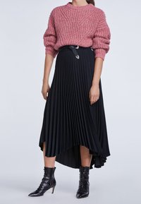 Rosa Strickpullover mit übergroßen Ärmeln, kombiniert mit einem schwarzen, gefalteten Rock mit asymmetrischem Saum und schwarzen Knöchelstiefeln.