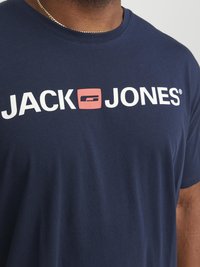 Camiseta de algodón azul marino con "JACK" en blanco y "JONES" en blanco con un acento cuadrado rojo, cuello redondo y manga corta.