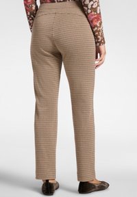 Hnědé a béžové kostkované kalhoty s úzkým střihem, vyznačující se vysokým pasem a plochým předním dílem. Nošeny s černými plochými botami.