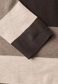Gros plan d'une manche de pull tricoté avec des rayures horizontales beige, marron clair et marron foncé.