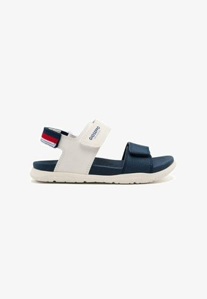 Sandalia ajustable en azul marino y blanco con correas de velcro, suelas texturizadas y un diseño ligero. Presenta un acento de correas en rojo y azul contrastantes.