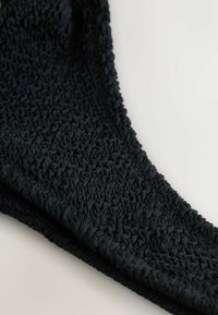 Țesătură neagră cu un design texturat, pliat. Materialul este moale, flexibil și are o finisare netedă, formând o formă curbată.