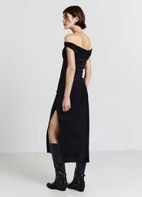 Schwarzes schulterfreies Kleid mit figurbetonter Silhouette, seitlichem Schlitz und glatter Textur, kombiniert mit kniehohen schwarzen Lederstiefeln.