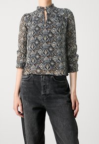 Blouse transparente à motifs dans des couleurs sombres avec un col haut et une ouverture en forme de clé, dotée de manches trois-quarts et d'un tissu texturé.