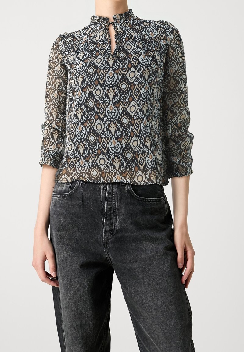 Blouse transparente à motifs dans des couleurs sombres avec un col haut et une ouverture en forme de clé, dotée de manches trois-quarts et d'un tissu texturé.