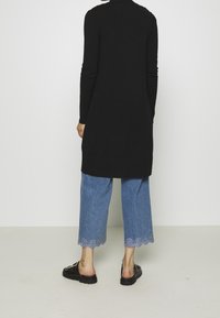 Túnica negra de manga larga con corte recto, combinada con jeans cortos de color azul claro con detalle de dobladillo en ondas. Sandalias negras tipo slip-on.