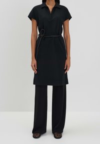 Czarna sukienka koszulowa z kołnierzykiem, krótkimi rękawami i paskiem w talii. Nosi się ją na szerokich czarnych spodniach i zestawia z czarnymi sandałami z siateczki.