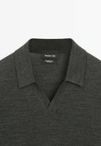 Mörkgrå merinoull polo-tröja med V-hals och plattstickad krage. Har en slät struktur och enkel design. Varumärkesetikett synlig.